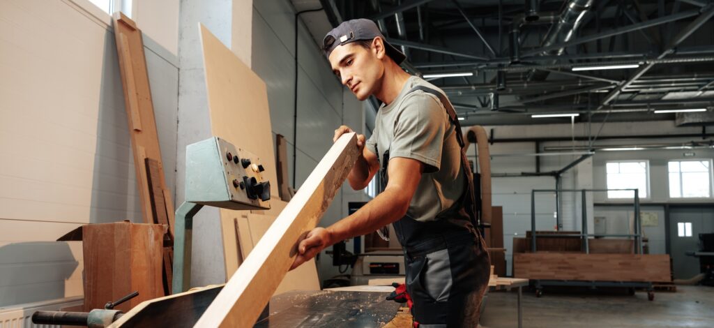 Young carpenter working on woodworking machines in the furniture factory